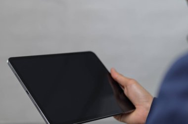 Bir kişi tableti boş bir ekranla tutuyor, minimalist bir arkaplanda. Görüntü, modern teknolojinin profesyonel ve gelişigüzel bir ortamda kullanılmasını sağlar..