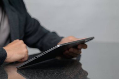 Cam sehpanın üzerinde şık bir tablet cihazı tutan birinin yakın plan görüntüsü. Görüntü modern teknolojiyi profesyonel bir ortamda yakalıyor, etkileşimi ve bağlantıyı vurguluyor..