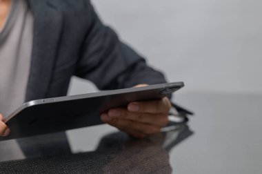 Gri ceketli bir adam modern bir çalışma alanında tablet tutuyor. Odak noktası eller ve cihaz, dijital etkileşimi vurguluyor.