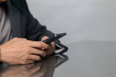 Yansıtıcı bir yüzeyde akıllı telefonu tutan ellerin yakın çekim görüntüsü. Görüntü, dijital iletişim ve modern yaşam tarzının bir anını yakalıyor..