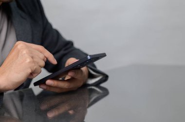 Bir insan şık cam bir masada otururken akıllı bir telefonla iletişim kurar. El hareketleri modern bir ortamda teknolojiyle aktif bir ilişki olduğunu gösteriyor..