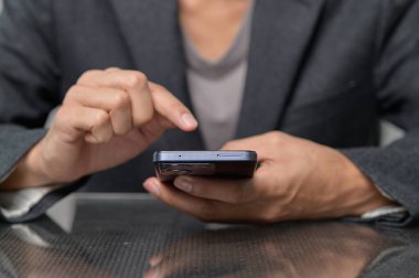Profesyonel bir çevrede modern teknolojiyi ön plana çıkaran akıllı telefon kullanan bir iş adamının yakın plan görüntüsü. Odak noktası eller ve cihaz etkileşimi..