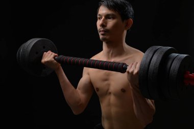 Kararlı bir adam ağır bir dambıl kaldırıyor, fiziksel güç ve zindelik gösteriyor. Koyu arkaplan, odaklanmış ifadesini ve kas yapısını vurguluyor..