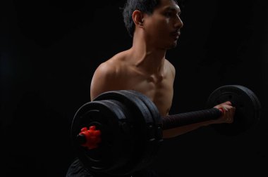 Kendini adamış bir birey karanlık bir ortamda halter kaldırarak güç eğitimine ve kişisel sağlığına olan bağlılığını gösterir. Odaklanma ve çabayı vurgular.