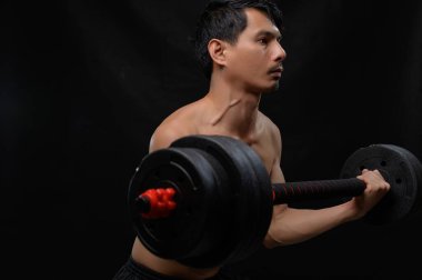 Odaklanmış bir sporcu ağırlık kaldırma antrenmanına katılır, sağlık ve zindeliğe olan bağlılığını gösterir. Koyu arkaplan egzersiz alanına yoğunluk ekler.