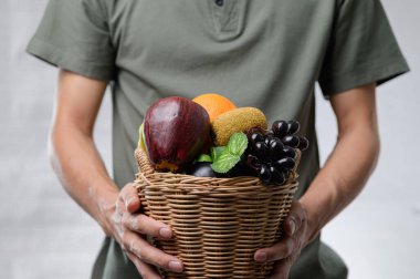 Bir adam içi taze ve renkli meyvelerle dolu dokuma sepetini sunar. Sahne sağlıklı yaşam ve doğal gıda seçeneklerini vurguluyor..