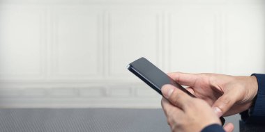 Bir bireyin elinde akıllı telefon tutarken, tarafsız bir arkaplan karşısında modern teknoloji ve iletişim sergilenirken yakın plan görüntüsü..