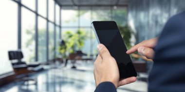 Modern ofis ortamında bir iş adamı cep telefonuyla iletişim kurar. Gösterişli tasarım ve cam mimarisi profesyonel bir atmosfer yaratıyor..