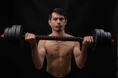 Odaklanmış genç bir adam dambılı güçlü bir pozda kaldırır, kararlılık ve zindeliğe bağlılığını gösterir. Güç ve sağlık gelişimi konuları için ideal.