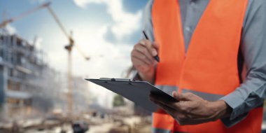 Güvenlik yeleği giymiş bir inşaat işçisi, inşaat sektöründe güvenliğe ve organizasyona olan bağlılığını vurgulayan bir iş yerinde bir pano tutuyor..