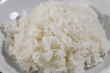 Bu resim, kabarık dokusunu sergileyen bir kase taze pişmiş beyaz pirinç içeriyor. Yemek için idealdir, çeşitli mutfaklarda önemli bir malzemeyi vurgular..