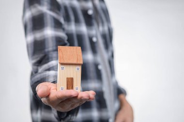 Ekose gömlek giyen bir kişi küçük ahşap bir model evi elinde tutar. Bu görüntü ev, yatırım ve gayrimenkul mülkiyeti kavramını sembolize ediyor. Mimari ya da yaşam tarzı temaları için mükemmel.