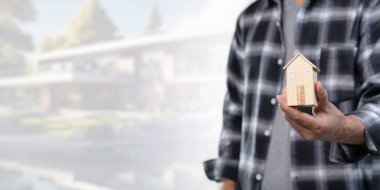 Konut kiralama ve satma konseptini araştırın. Bu resim, emlak yatırımını ve piyasa dinamiklerini sembolize eden bir model evi tutan kişiyi gösteriyor..