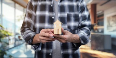 Konsept resim, kiralık konutların alınıp satılmasını, elinde minyatür bir ev modeli olan bir kişinin, emlak yatırımını sembolize ettiğini gösteriyor..