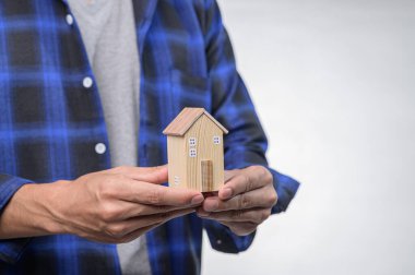 Bir insan, hayalleri ve tutkuları simgeleyen narin ahşap bir ev modeli taşır. Görüntü, ev tasarımının işçiliği ve basitliğine odaklanıyor..