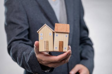 Bir işadamı, emlak yatırımı ve emlak fırsatlarını simgeleyen ahşap model evler sunuyor. Sunumlar veya finansal kavramlar için ideal.