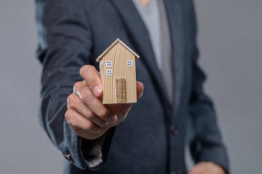 Bir işadamı, emlak piyasası ve yatırım fırsatlarına olan bağlılığını simgeleyen küçük ahşap bir ev modelini gururla sunar..