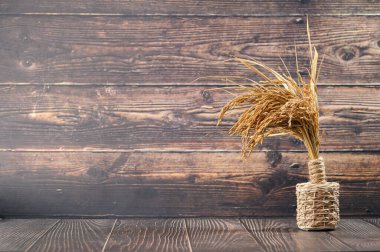 İpe sarılı vazodaki kurumuş otların eşsiz bir düzeni ahşap bir zemine karşı duruyor ve ev dekorasyonu için mükemmel bir ortam yaratıyor..