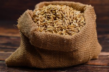 Taze kahverengi pirinç çuvalı, tahılın eşsiz dokusunu ve topraksı tonlarını gösteren ahşap bir masanın üzerinde oturur. Aşçılık projeleri için mükemmel..