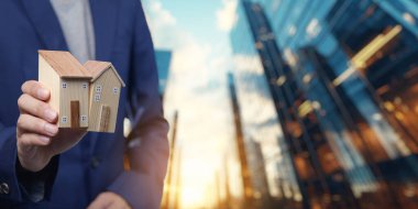 Kendine güvenen bir emlakçı, satın alma, satma ve konut kiralamanın dinamik yönlerini sembolize ederek şehir ortamında model evler sunar..