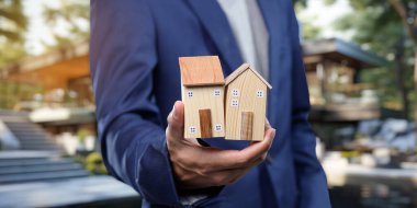 Bir profesyonel, gayrimenkul işlemlerini simgeleyen minyatür evler tutuyor. Bu resim konut satın alma, satma ve kiralama kavramlarını temsil etmektedir..