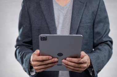 Gri takım elbiseli bir iş adamı modern ofis ortamında bir tablet tutuyor. İş yerinde teknoloji ve iletişim sergiliyor..