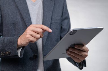 Bir iş adamı modern ofis ortamında bir tabletle ilgilenir, teknoloji etkileşimi ve çağdaş çalışma kültürü sergiler.