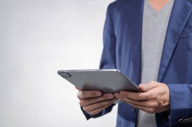 Bir kişi şık bir tasarım ile bir tablet tutar, şık bir ceket giyer ve rahat bir tişört giyer, minimal beyaz bir arkaplan kullanır, modern teknoloji kullanımı için idealdir..