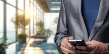 Gösterişli takım elbiseli bir işadamı, akıllı telefonuyla çağdaş bir ofiste karşılaşır. Güneş ışığı geniş pencerelerden akar ve verimli bir atmosfer yaratır..