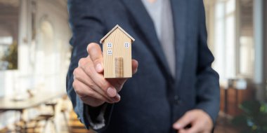 Ahşap ev modelini sunan bir işadamı gayrimenkul satışını ve pazarlığı simgeliyor. Bu zarif ofis, profesyonelliği ve başarıyı temsil ediyor..