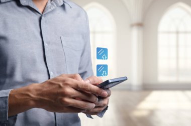 Bir çalışan dijital verileri yüklemek ve indirmek için bir cep telefonu kullanıyor, modern teknolojiyi ve işyerindeki kusursuz iletişimi simgeliyor.