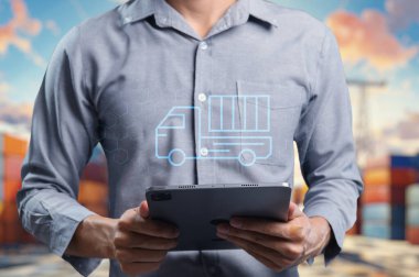 Kamyon simgesini gösteren bir tablet tutan bir kişi, ithalat ve ihracat operasyonlarına odaklı küresel ticaret ve lojistik kavramları sembolize ediyor.