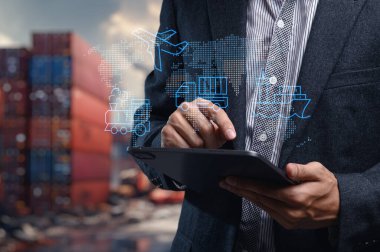 Bir kişi ithalat ve ihracat alanında küresel ticaret kavramlarını keşfetmek için bir tablet kullanır. Görsel öğeler arasında nakliye simgeleri ve modern bir iş yaklaşımı için dijital bir harita yer alıyor.