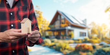 Konut kiralama ve satma kavramını araştırın, resimli bir açık hava ortamında bir kişinin elinde bir model ev sergileyin..