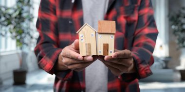 Bu resim, konut kiralama ve satma kavramını, model evleri elinde bulunduran kişiyi, emlak yatırımını ve mülkiyetini sembolize eden kişiyi gösteriyor..