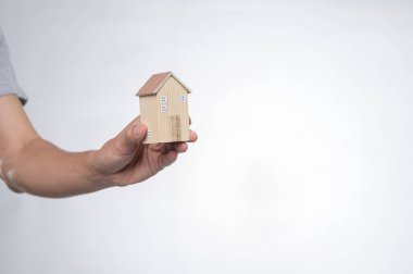 Bir el, ev ve konut kavramlarını sembolize eden küçük ahşap bir ev modeli sunar. Tarafsız bir zemine karşı minimalist tasarım yaratıcılığı ve sıcaklığı vurgular..