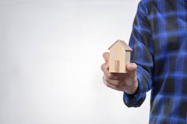 Bir kişi ev sahipliği ve emlak yatırımını sembolize eden küçük ahşap bir model ev tutuyor. Tarafsız arka plan modelin tasarımını vurgular.