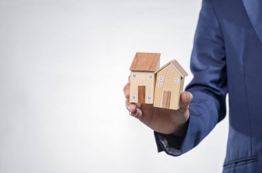 Takım elbiseli bir kişi, emlak piyasası ve mülkiyet ve ev tasarımı alanlarındaki yatırım fırsatlarını sembolize eden iki model ahşap ev tutuyor..