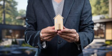Profesyonel bir insan, emlak satışları ve ev yatırımlarını sembolize eden küçük bir model ev sunar. Havalı dış mekan konsepte zarafet katıyor..