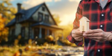 Görüntü, sonbahar arkaplanına karşı model ev tutan bir kişinin yatırım ve gayrimenkul kararlarını sembolize ettiği kiralık konut satın alma ve satma kavramını gözler önüne seriyor..