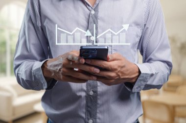 Bir adam akıllı telefonuyla uğraşırken, grafik örtüşmesi, parlak ve modern bir ofiste, veri odaklı karar verme sürecini sembolize eden eğilimleri ve ölçümleri gösterir..