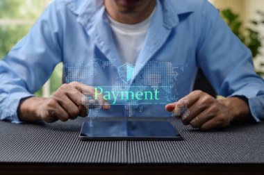 Bir kişi dijital güvenlik grafiği içeren çevrimiçi ödeme yapmak için tabletle etkileşime girer. Bu resim modern finansal işlemleri ve teknolojiyi temsil ediyor..