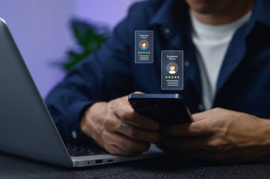Bir kişi, modern dijital iletişim ve uzaktan çalışma dinamiklerini gösteren bir dizüstü bilgisayar üzerinde çalışırken müşteri değerlendirmelerini görmek için akıllı telefon kullanır..