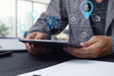Bu resim ithalat ihracat sektöründeki modern bir lojistik ve ulaşım sistemini gösteriyor. Bir kişi verileri yönetmek ve işlemleri verimli bir şekilde düzenlemek için bir tablet kullanır.
