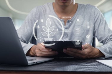 Bir insan mobil bir cihaza bağlanıyor, bahçe sezgileri ve bitki bakım aletleri keşfediyor. Ayar, modern teknolojinin kapalı alanda bahçe yapma uygulamalarını geliştirdiğini gösteriyor.