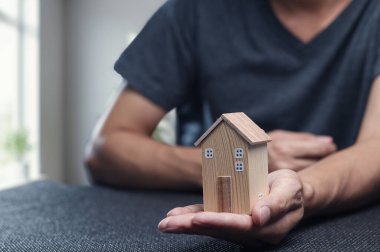 Mülk ticareti ve gayrimenkul yatırım fırsatlarının heyecan verici dünyasını simgeleyen küçük ahşap bir ev modelini elinde tutan bir kişi..