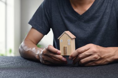 Mülk ticaretini sembolize eden bir model ev tutuyor. Bu resim gayrimenkul yatırımı, piyasa pazarlığı ve ev sahipliği stratejileri temalarını iletir.