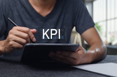 Bir kişi, modern bir çalışma alanındaki dijital tablet üzerinde temel performans göstergelerini analiz eder, iş stratejisini ve görsellerle veri odaklı karar verme mekanizmasını geliştirir.