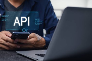 Bir geliştirici, modern programlama tekniklerini gösteren bir dizüstü bilgisayar kullanarak mobil API arayüzü ile etkileşime girer. Bu görüntü teknolojideki yenilikleri vurguluyor.