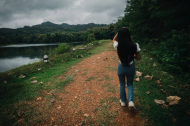 Bir kadın, yemyeşil yemyeşil bir göl kenarında güzel bir patika boyunca yürür. Bu sakin açık hava sahnesi sükunetin ve doğanın özünü yakalıyor..
